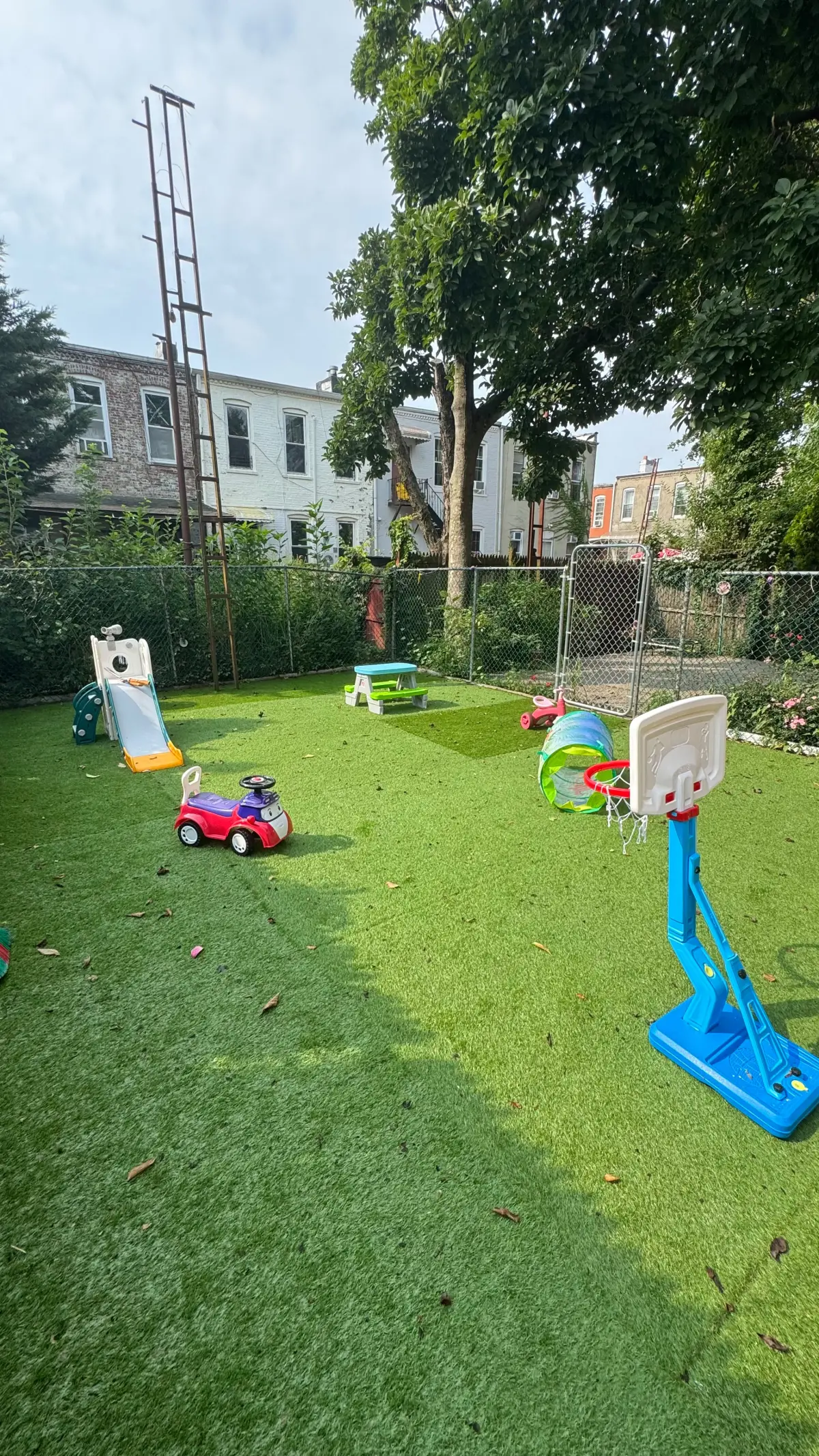 Patio trasero con juegos infantiles, canasta de básquet y césped verde