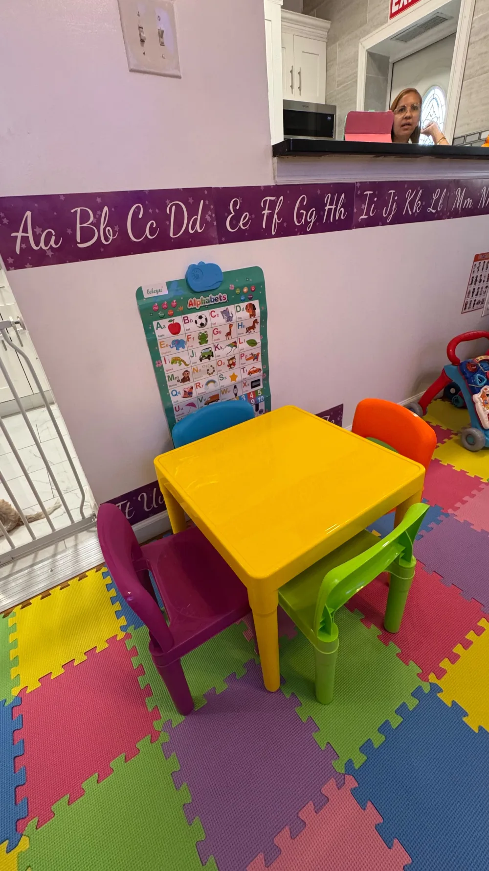 Mesa amarilla con sillas de colores y pared con abecedario, área de 3-K